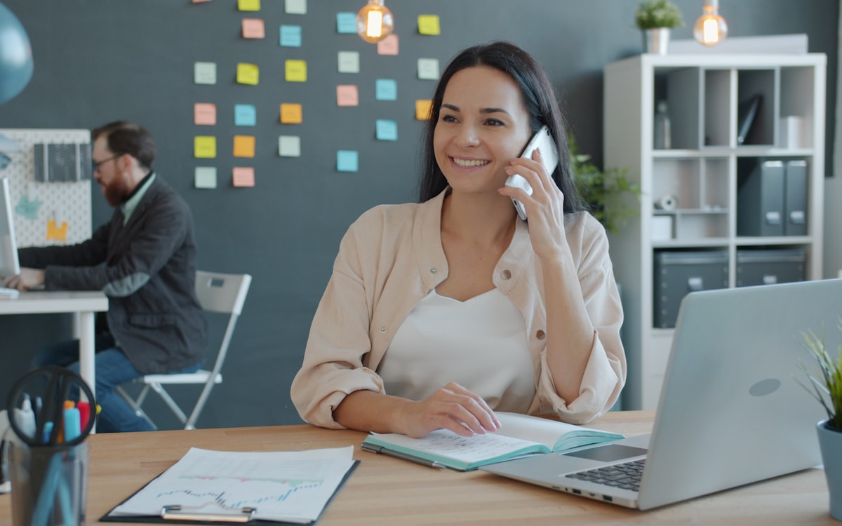 Atendente sorrindo ao telefone em frente ao computador fazendo follow-up de vendas com clientes