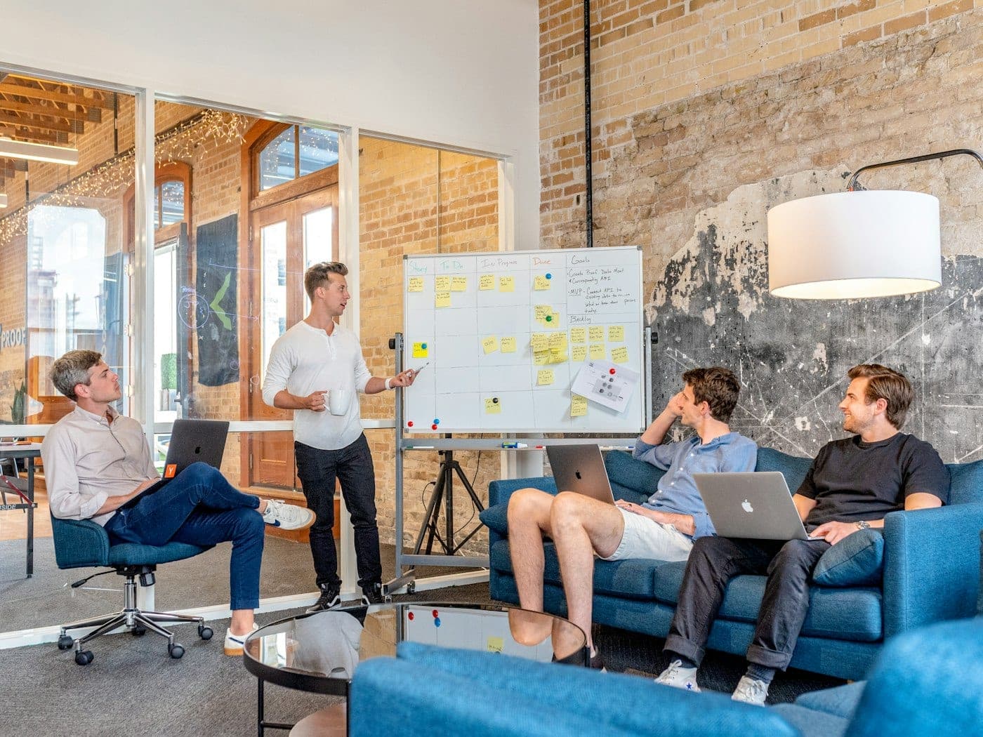 Equipe de 4 pessoas em escritório moderno, com homem apresentando um quadro kanban com post-its coloridos organizados em colunas — representando funil de vendas visual em CRM