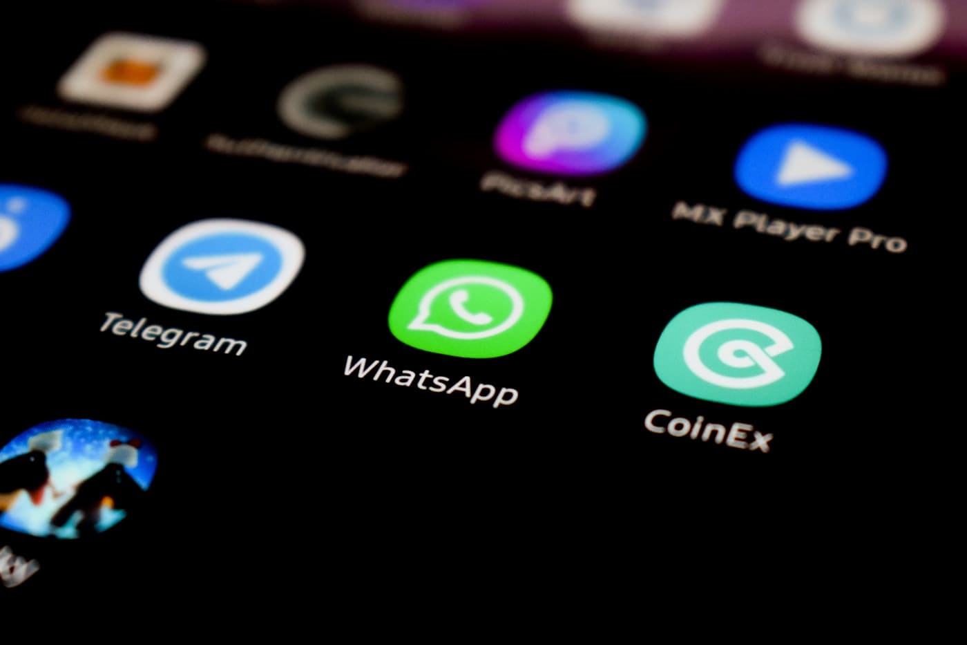 Tela de celular com ícones de aplicativos onde destaca o ícone verde do WhatsApp ao centro, ao lado de Telegram e CoinEx